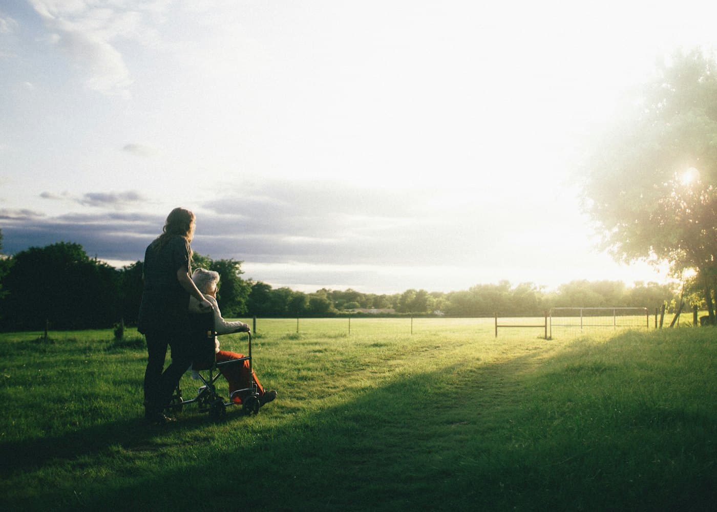 A caregiver walking beside a woman in a wheelchair outdoors